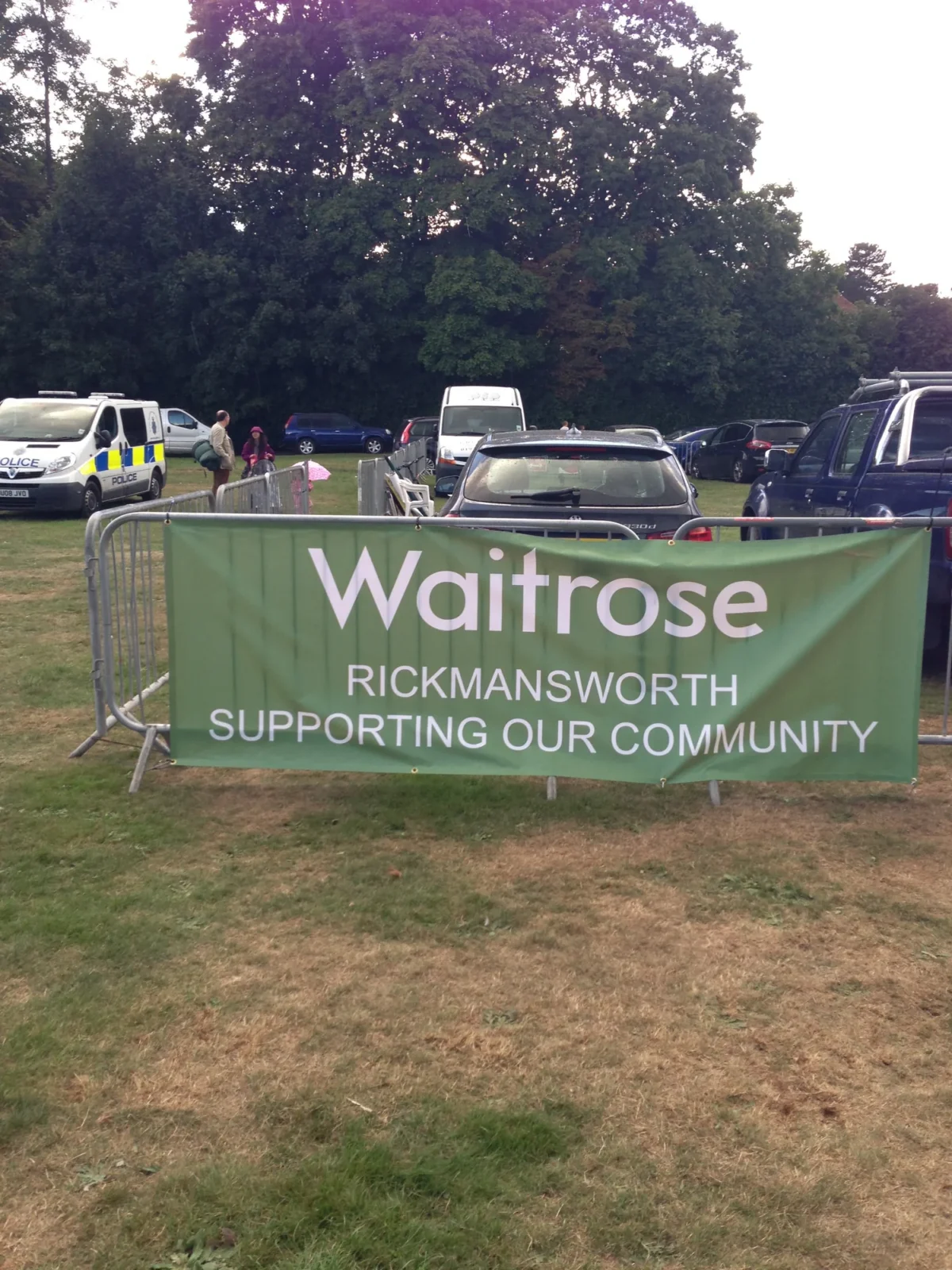 Waitrose Rickmansworth community banner beside parked vehicles and police van