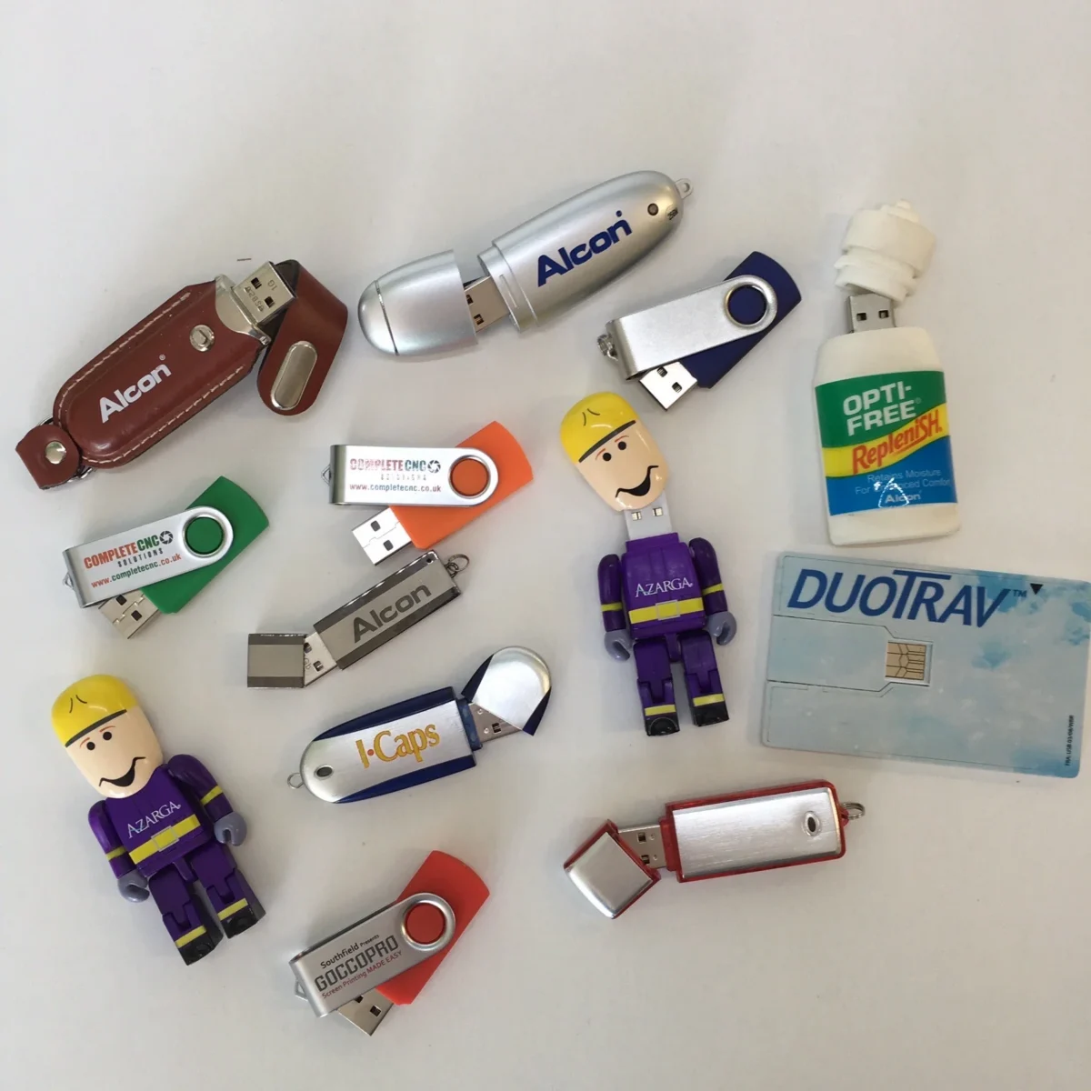 Assorted branded promotional USB flash drives on white background