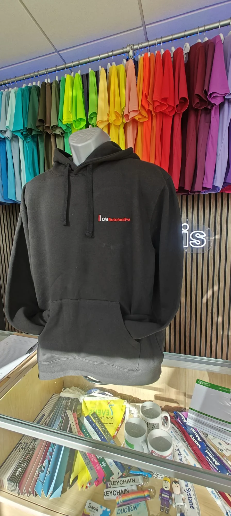 Black branded hoodie mannequin beside brightly coloured fabric rolls