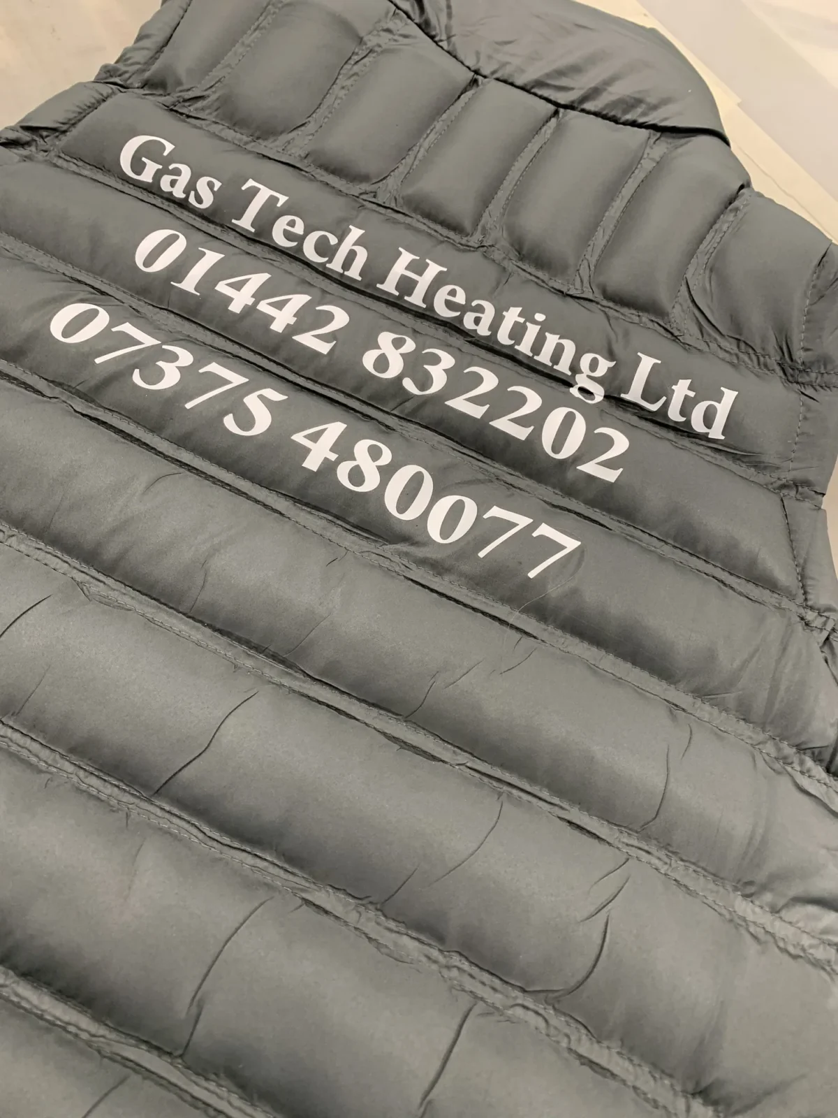 Black padded jacket printed with Gas Tech Heating contact details