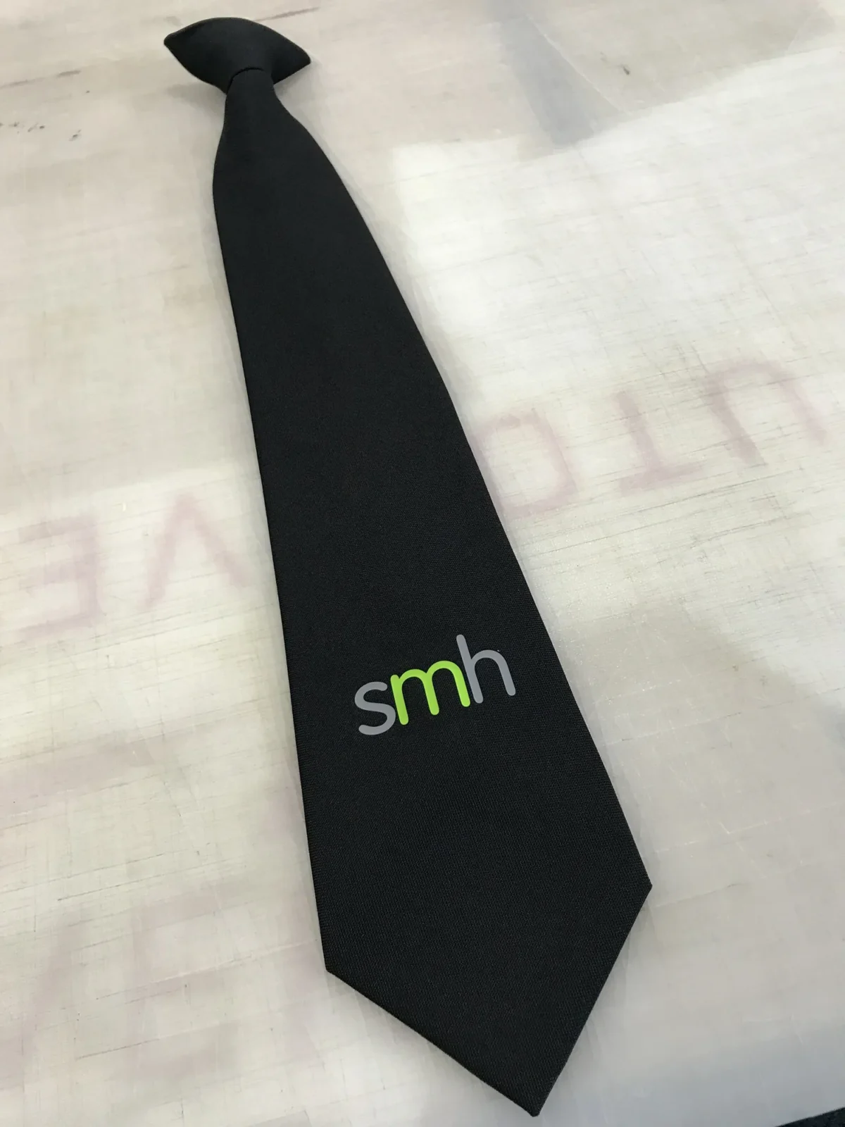 Black necktie with green and grey SMH logo
