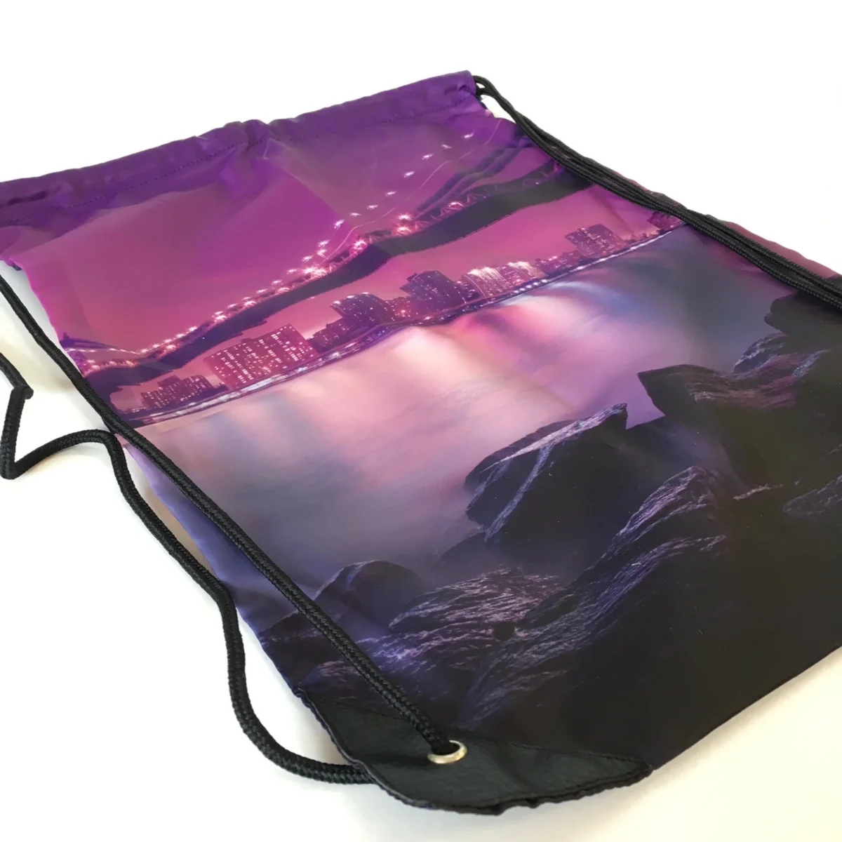Purple drawstring bag with illuminated cityscape and rocky shoreline print