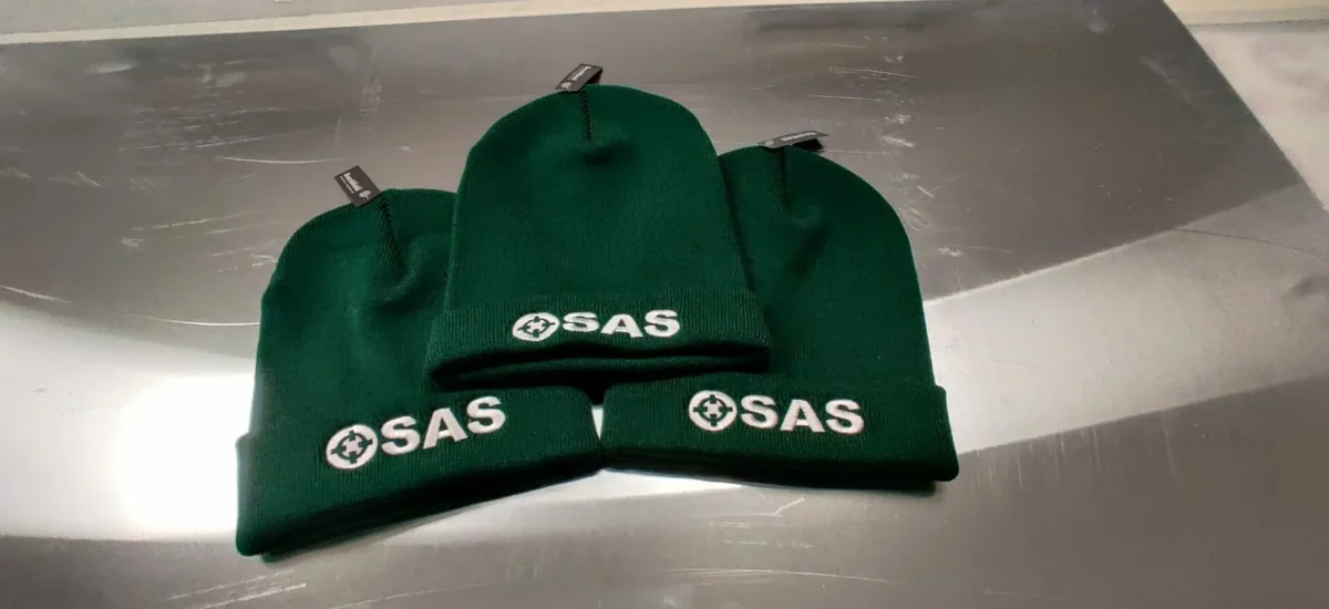 Three dark green SAS branded knitted beanies
