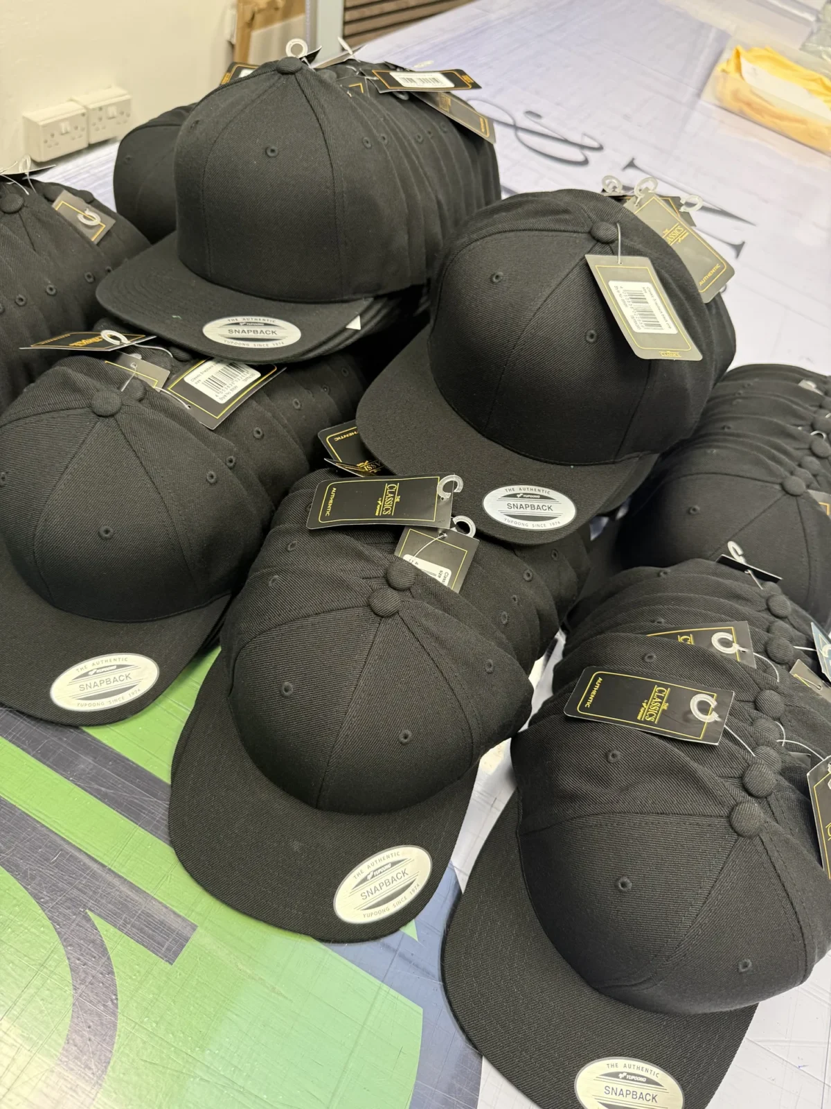 Pile of black snapback caps with retail tags