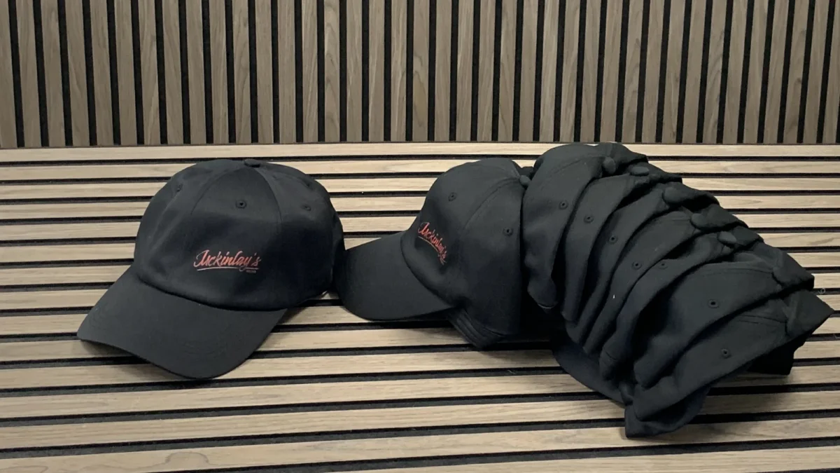 Black embroidered baseball caps stacked on wooden slatted bench