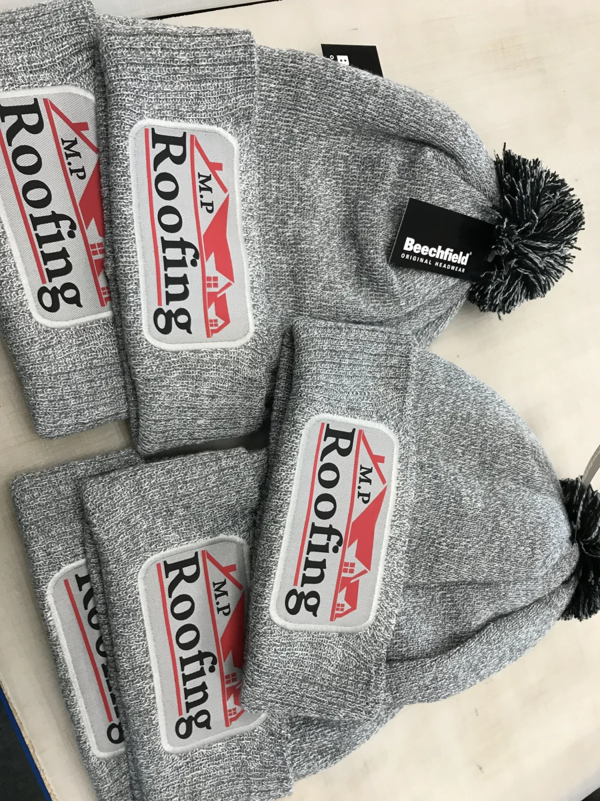 Grey Roofin g branded beanie hats with black pom-poms