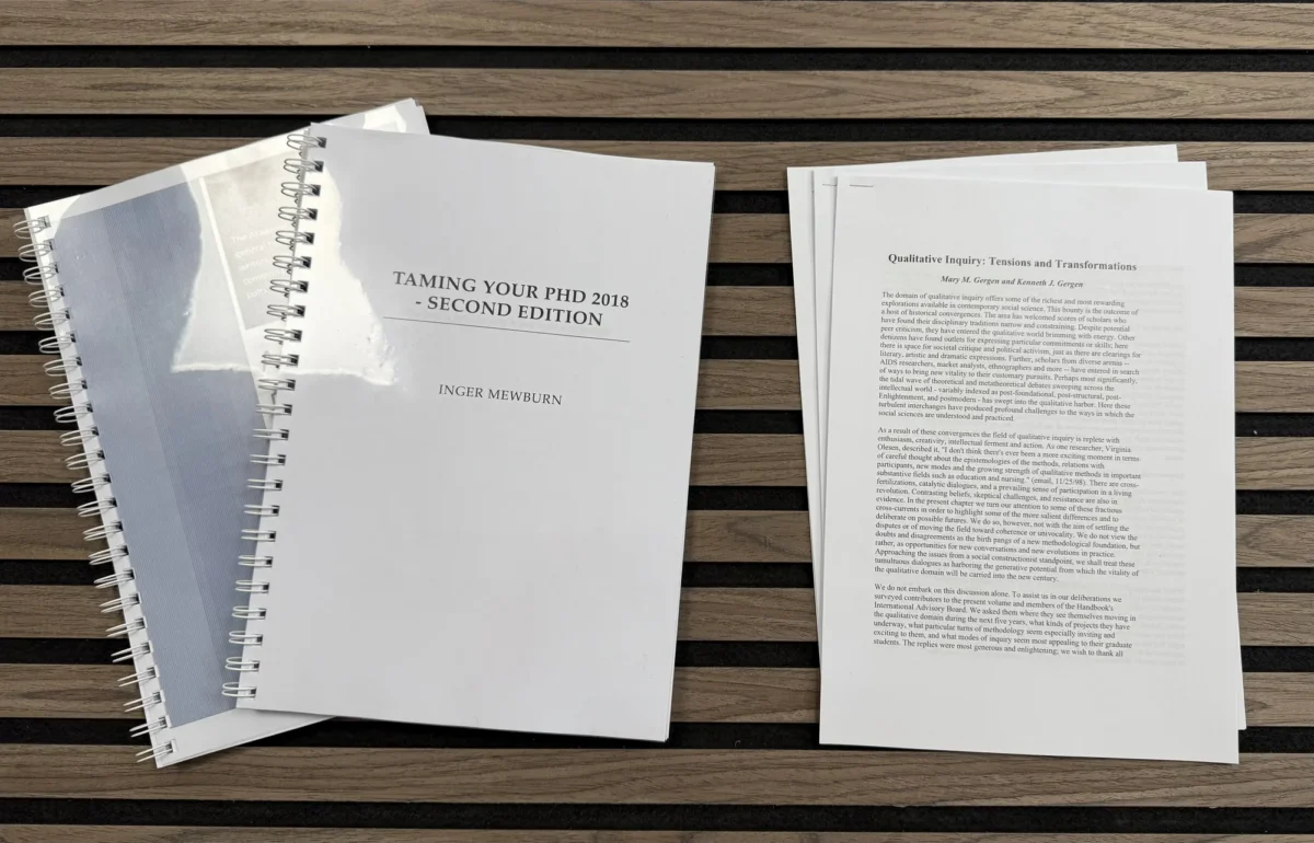PhD guidebook, notebooks and academic article on wooden table