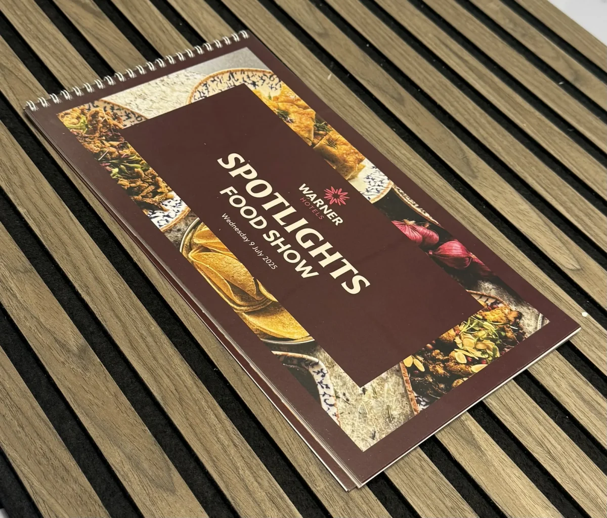 Warner Hotels spotlight food show brochure on wooden slatted table