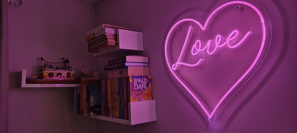 Pink neon love heart sign above shelves of books