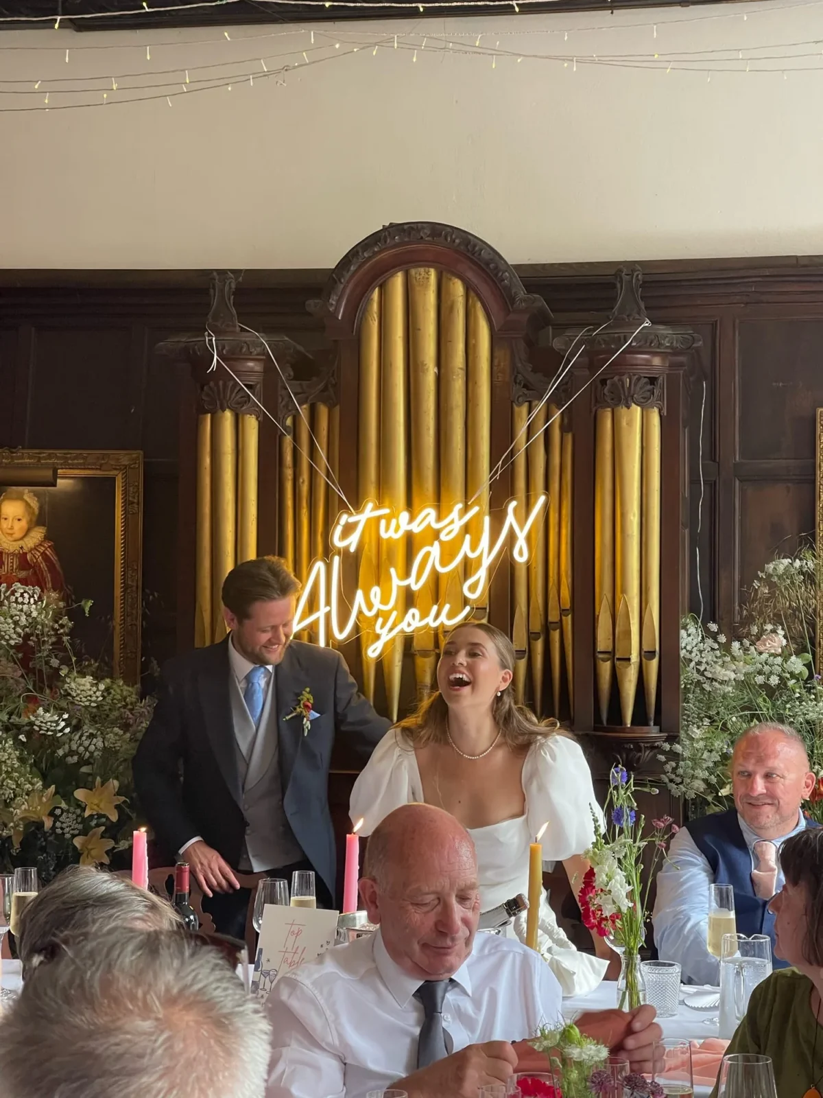 Bride and groom laughing at wedding reception beneath neon sign