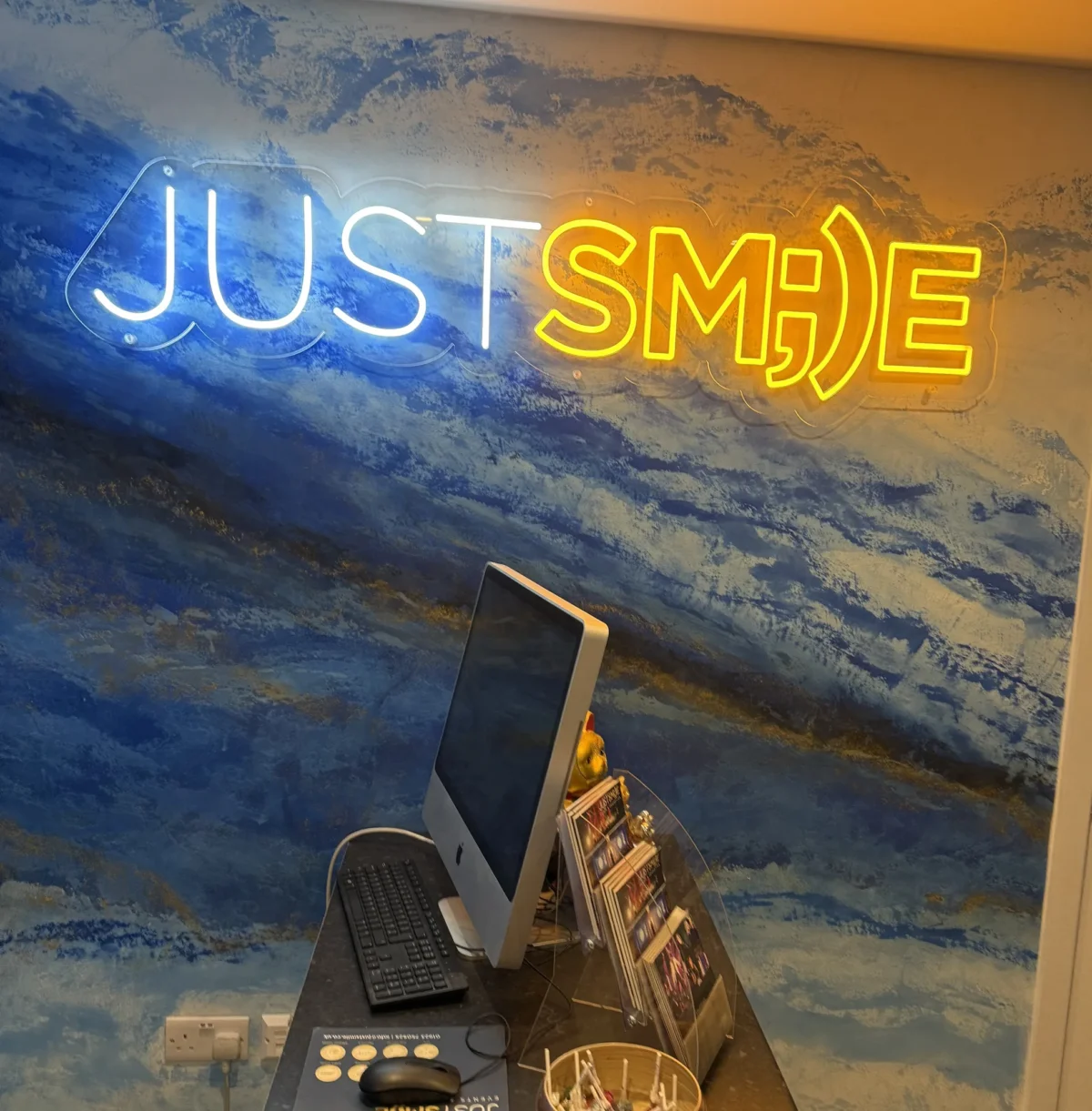 Neon “Just Smile” sign above a computer desk