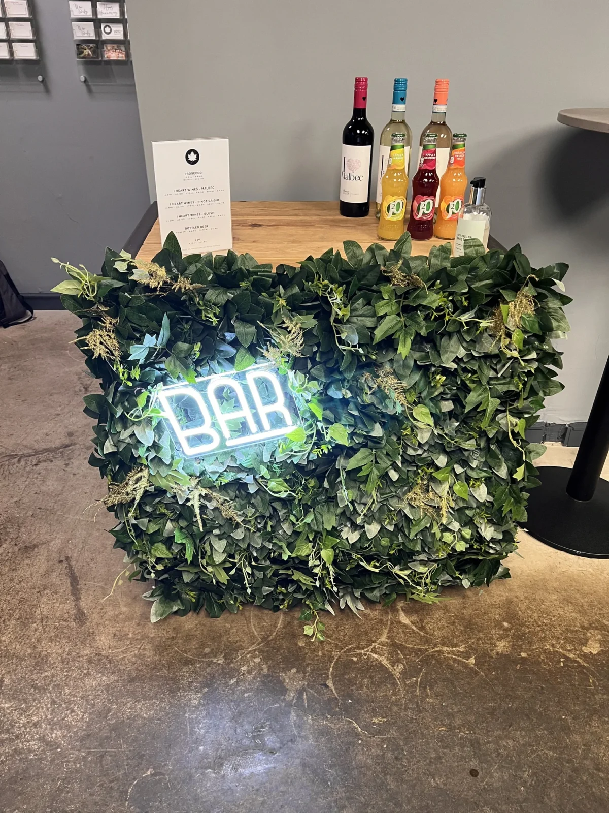 Leaf-covered bar counter with neon sign and bottled drinks