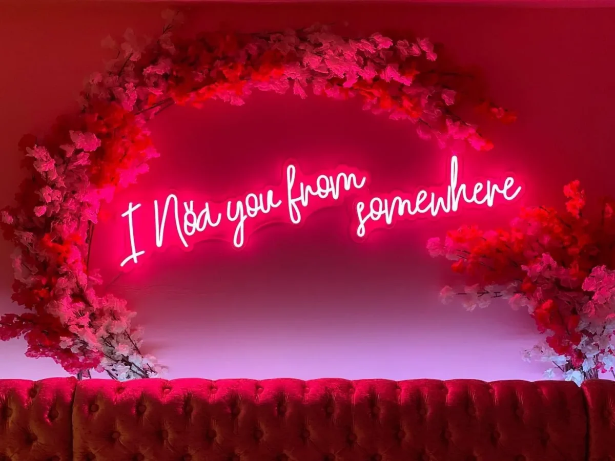 Pink neon sign reading ‘Meet you from somewhere’ beneath flowers
