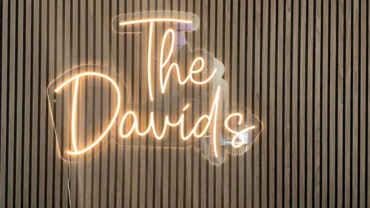 Illuminated 'The Davids' neon sign on wooden slatted wall