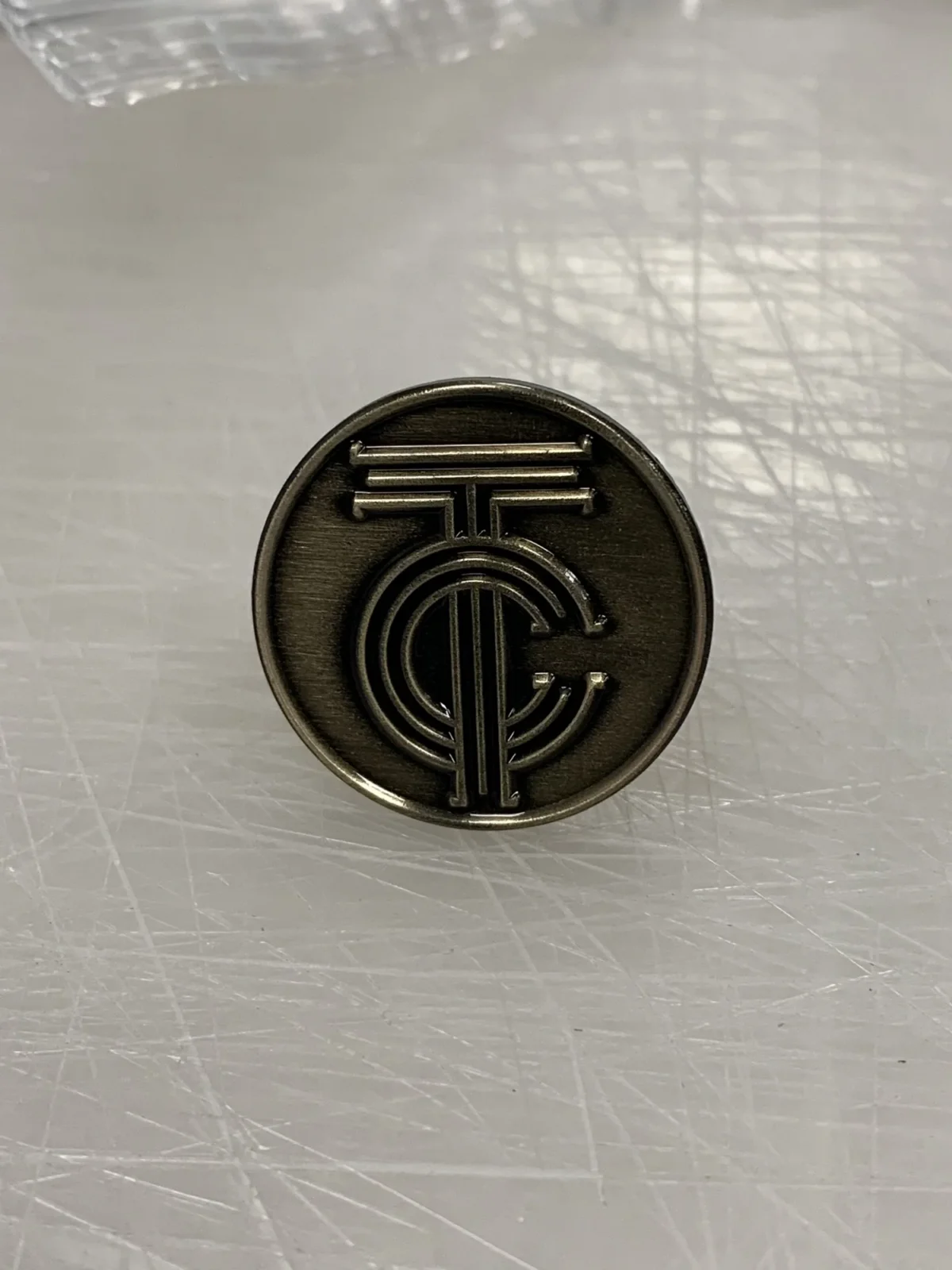 Dark metal coin featuring an embossed geometric emblem