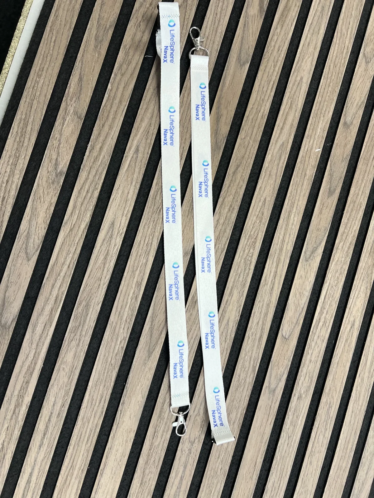 White LifeSphere NavaX lanyard with metal clips on wooden slats