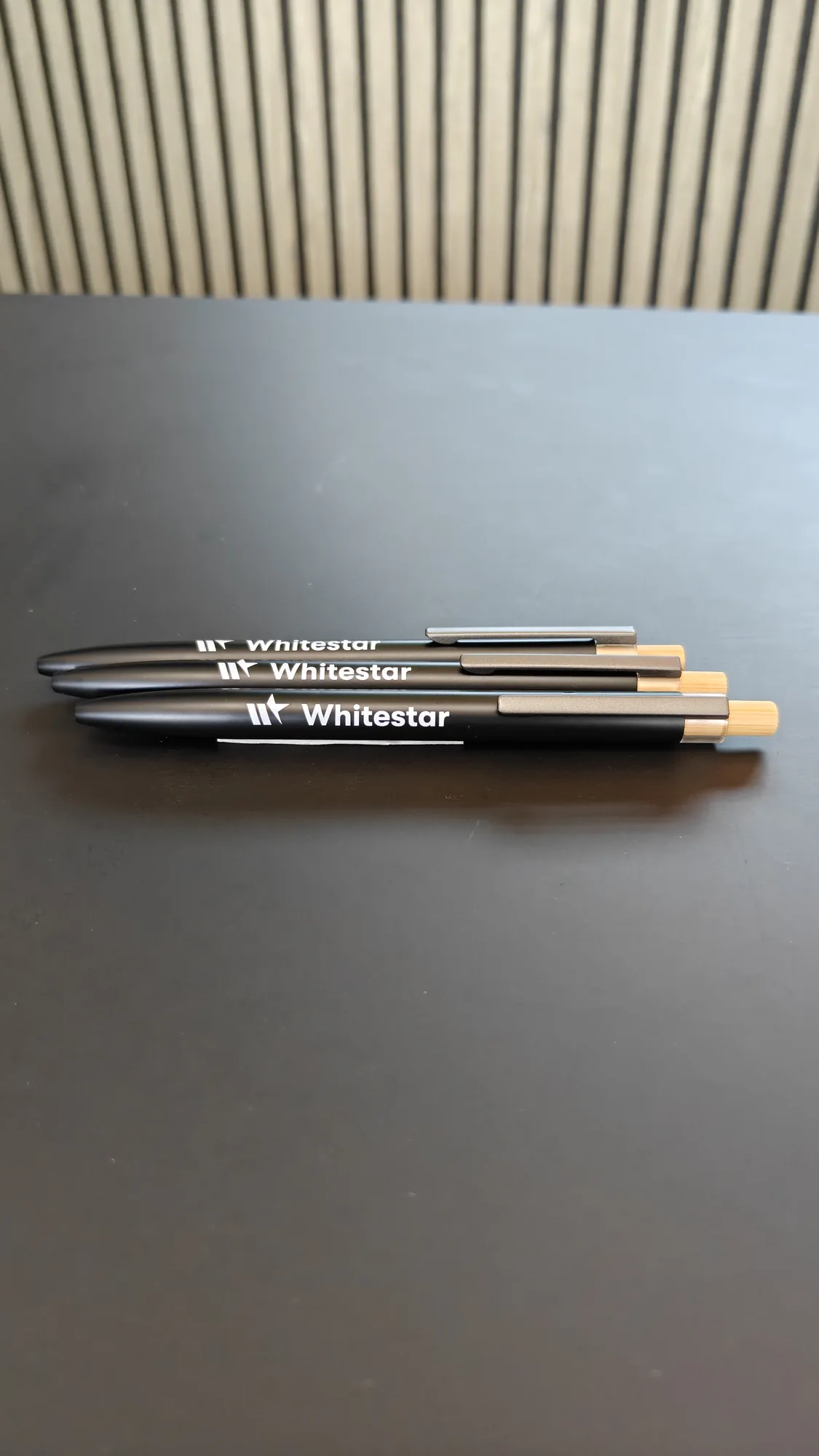 Three Whitestar branded black pens on a dark desk