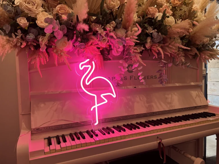 Piano beneath flowers and glowing pink flamingo neon sign
