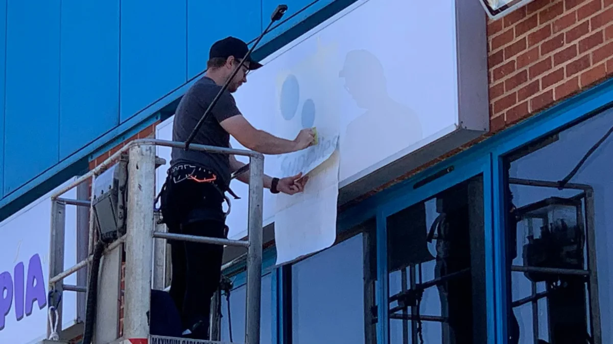 Worker removes sign covering from building using elevated platform