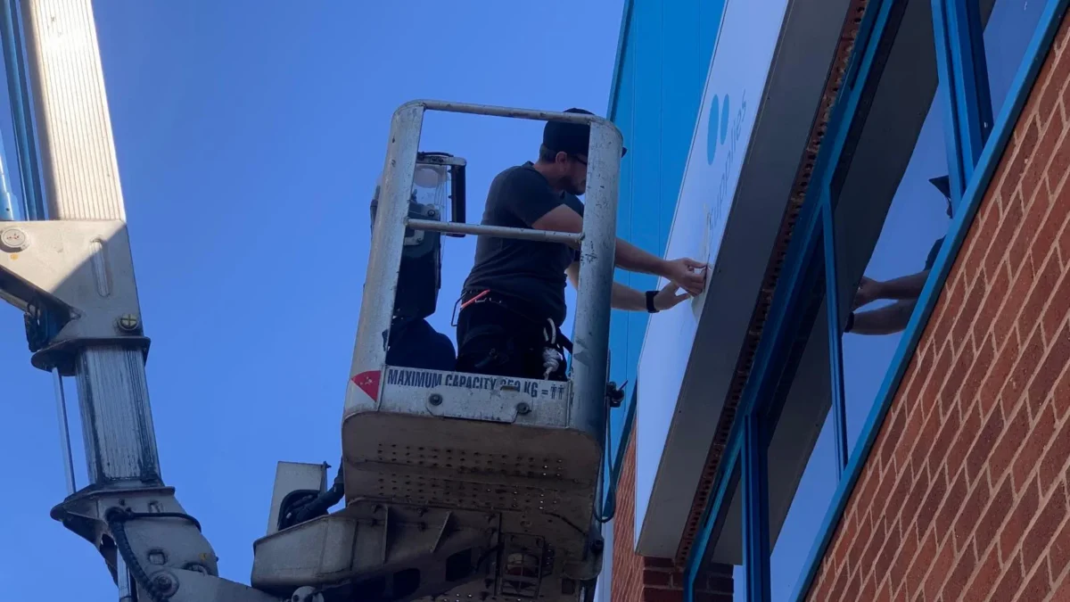 Worker in cherry picker installing shop signage