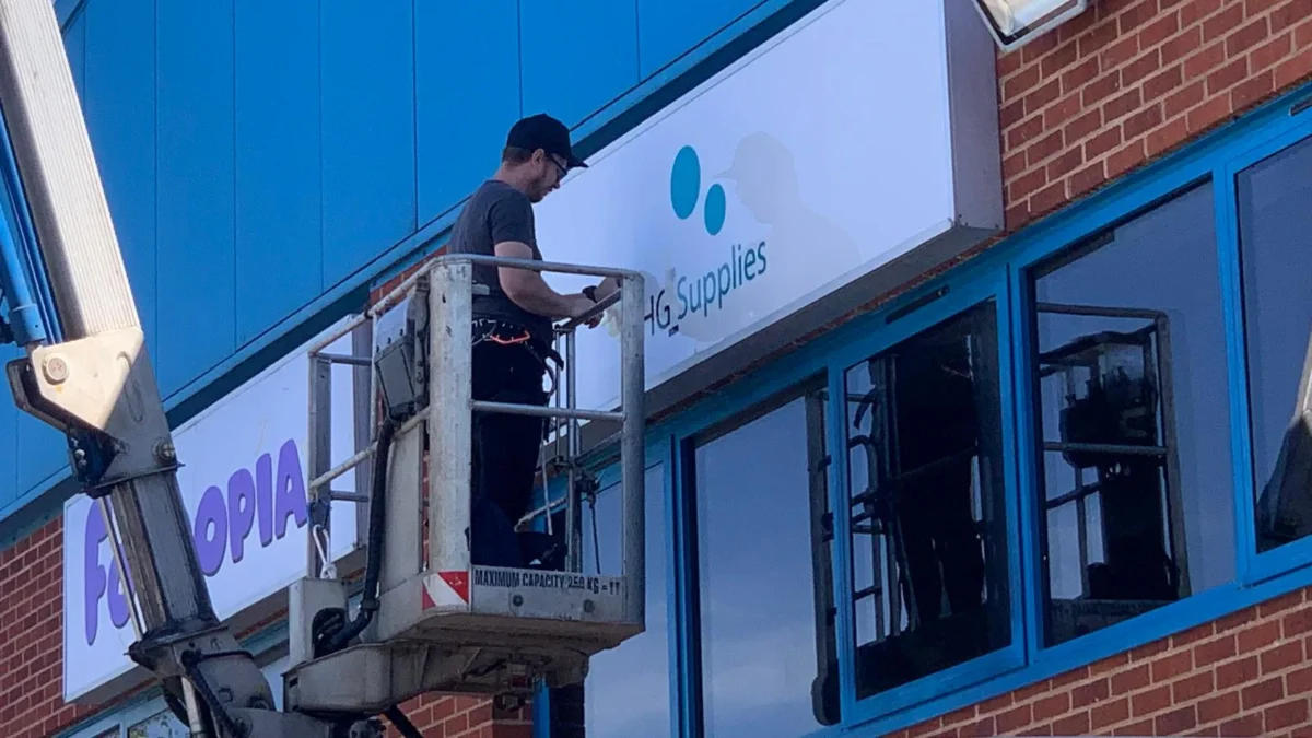 Worker installing HG Supplies sign from elevated platform