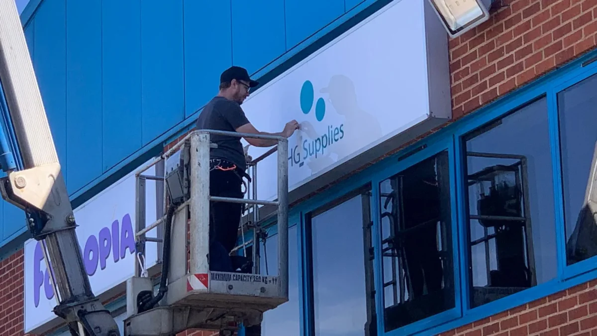 Worker installs HG Supplies sign from cherry picker
