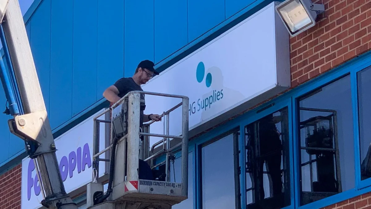 Worker on lift installing sign above shopfront