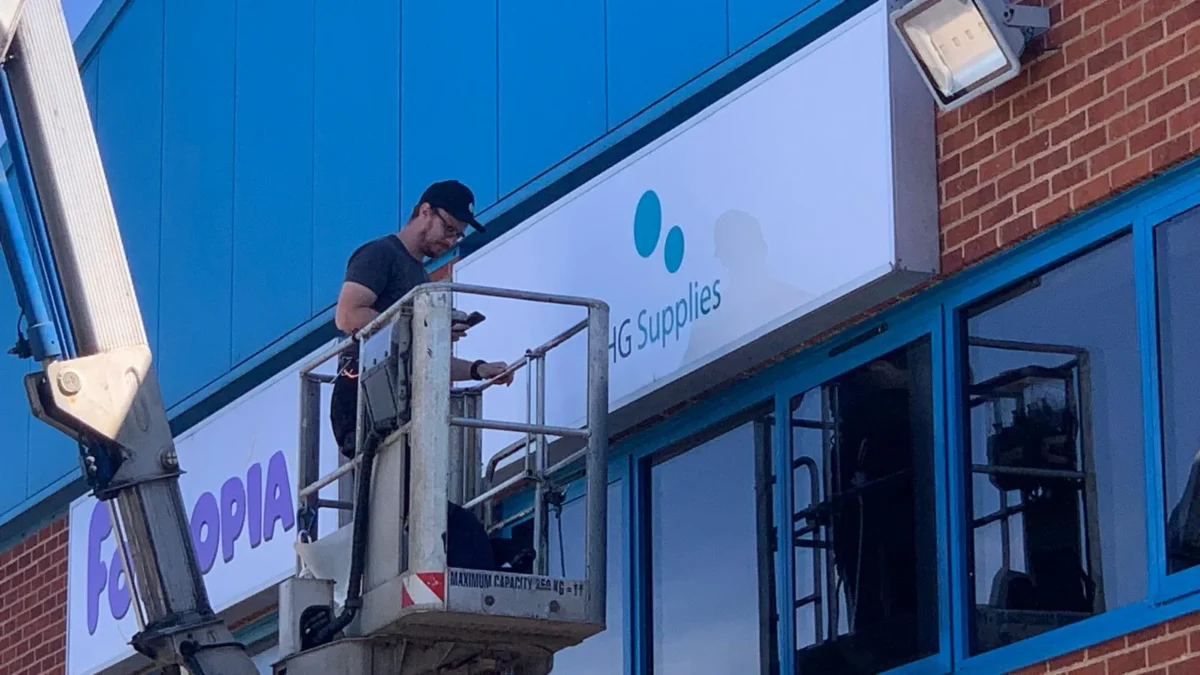 Worker installing signage from elevated platform outside commercial building