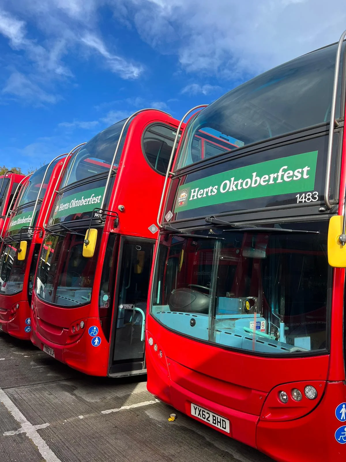 Red double-decker buses advertising Herts Oktoberfest under blue sky